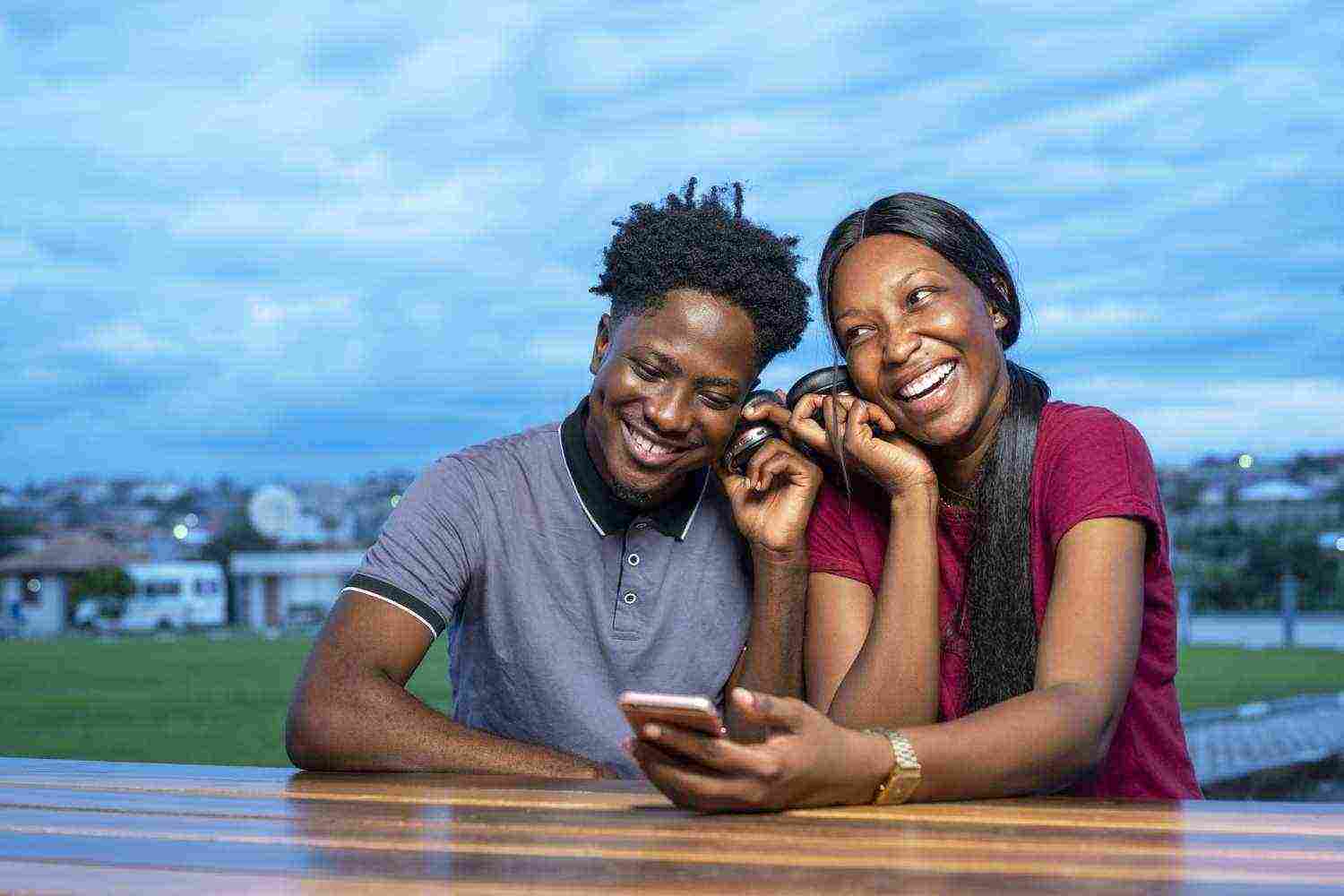 cute african couple sitting park watching funny video together