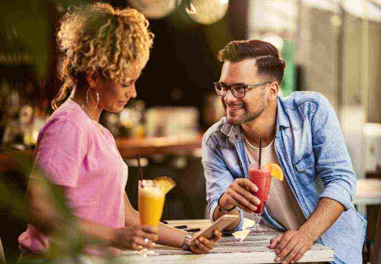 young smiling couple relaxing drinking fruit cocktails cafe woman is text messaging mobile phone