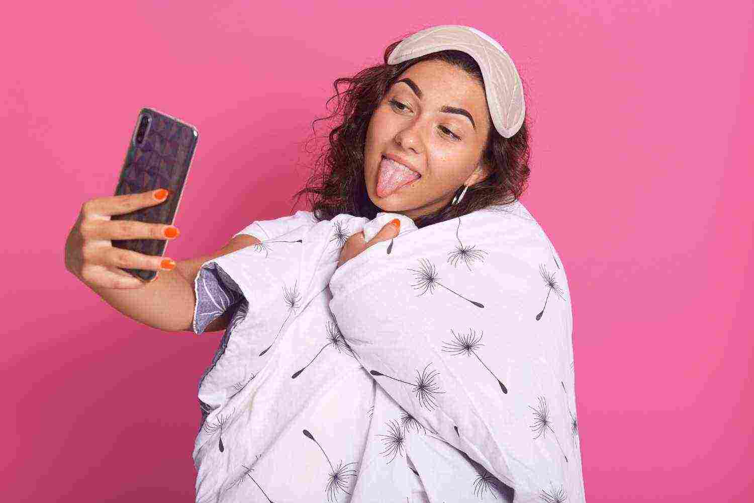 close up portrait happy female wrapped white blanket with dandelion showing her tongue making selfie