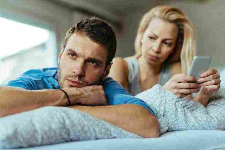 displeased man lying bed ignoring his girlfriend who is text messaging mobile phone1