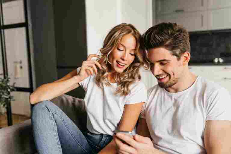 happy couple with smart phone looking screen smiling home portrait two young people enjoying day together reading good news