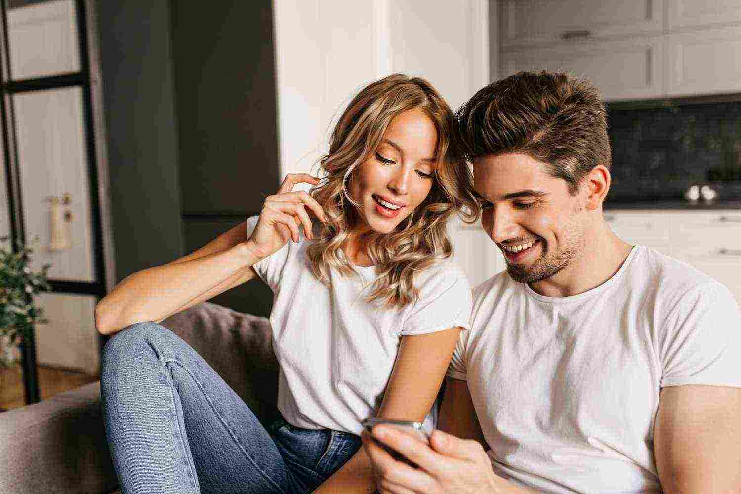 happy couple with smart phone looking screen smiling home portrait two young people enjoying day together reading good news