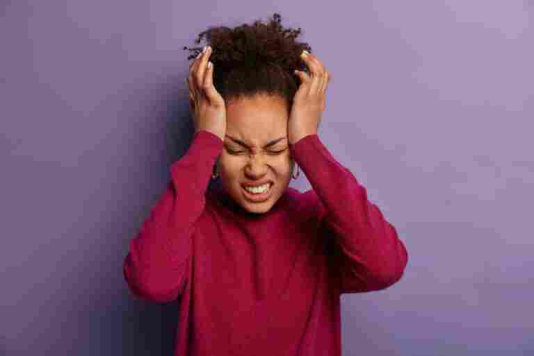 photo dissatisfied woman keeps hands temple suffers from unbearable headache clenches teeth with pain being exhausted after work wears burgundy turtleneck isolated purple wall