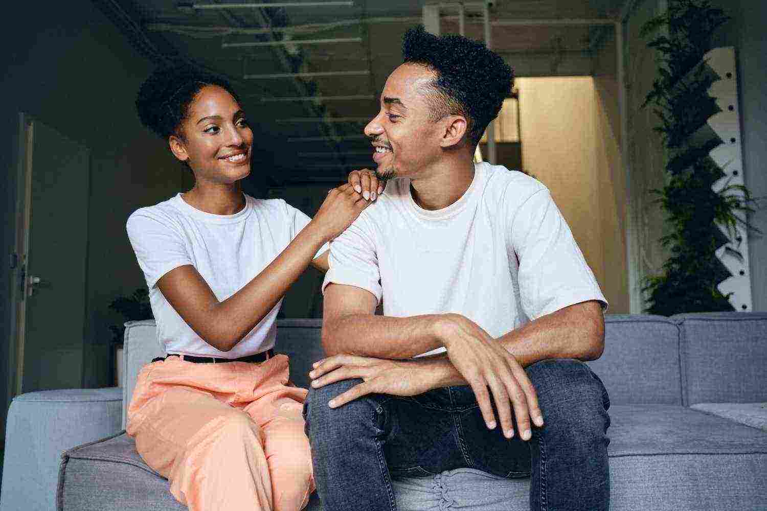 young attractive cheerful casual african american couple happily looking each other sofa modern home1