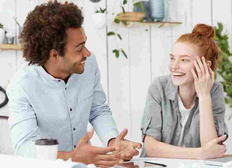 beautiful young redhead woman designer laughing jokes her cheerful dark skinned male colleague