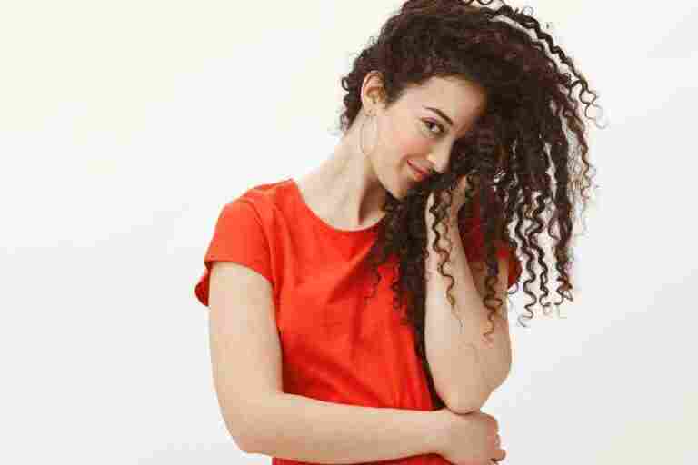 blushing flirty woman red dress covering half face with curly hair staring with one eye