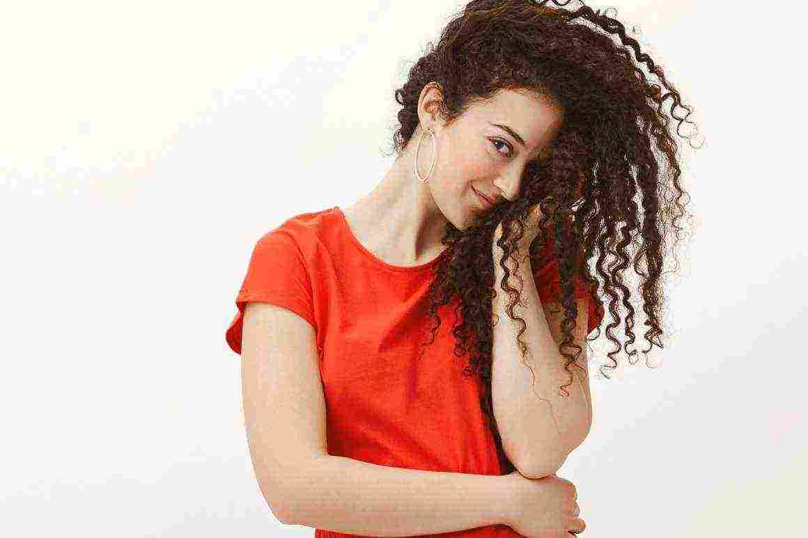blushing flirty woman red dress covering half face with curly hair staring with one eye