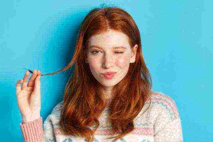 closeup cheeky redhead girl playing with hair strand winking smiling camera standing