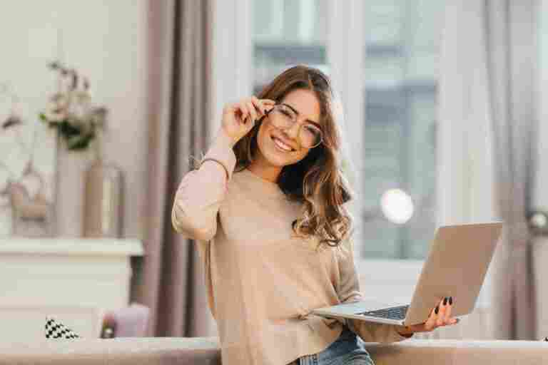 cute girl beige shirt touching glasses holding laptop with smile