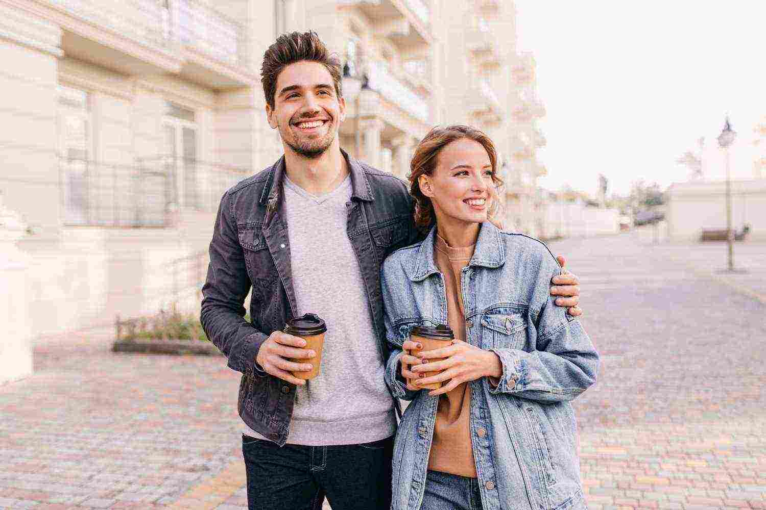 handsome young man holding cup coffee embracing girlfriend smiling couple enjoying outdoor date