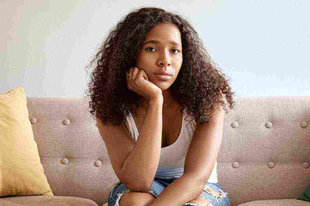 horizontal shot fashionable young african female with voluminous hairstyle having bored look has stay home because bad rainy weather sitting gray couch alone people lifestyle