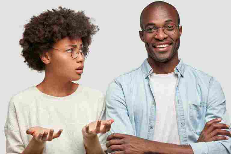 why are you laughing displeased african american female looks her husband who smiles broadly keeps hands crossed express different emotions stand closely each other isolated white wall