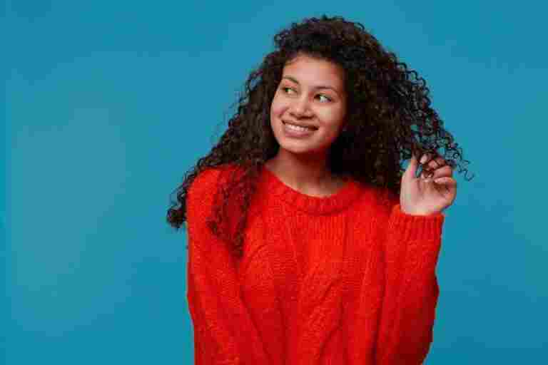 portrait beautiful lady with curly dark hair red knitted sweater holds strand hair her hand smiling