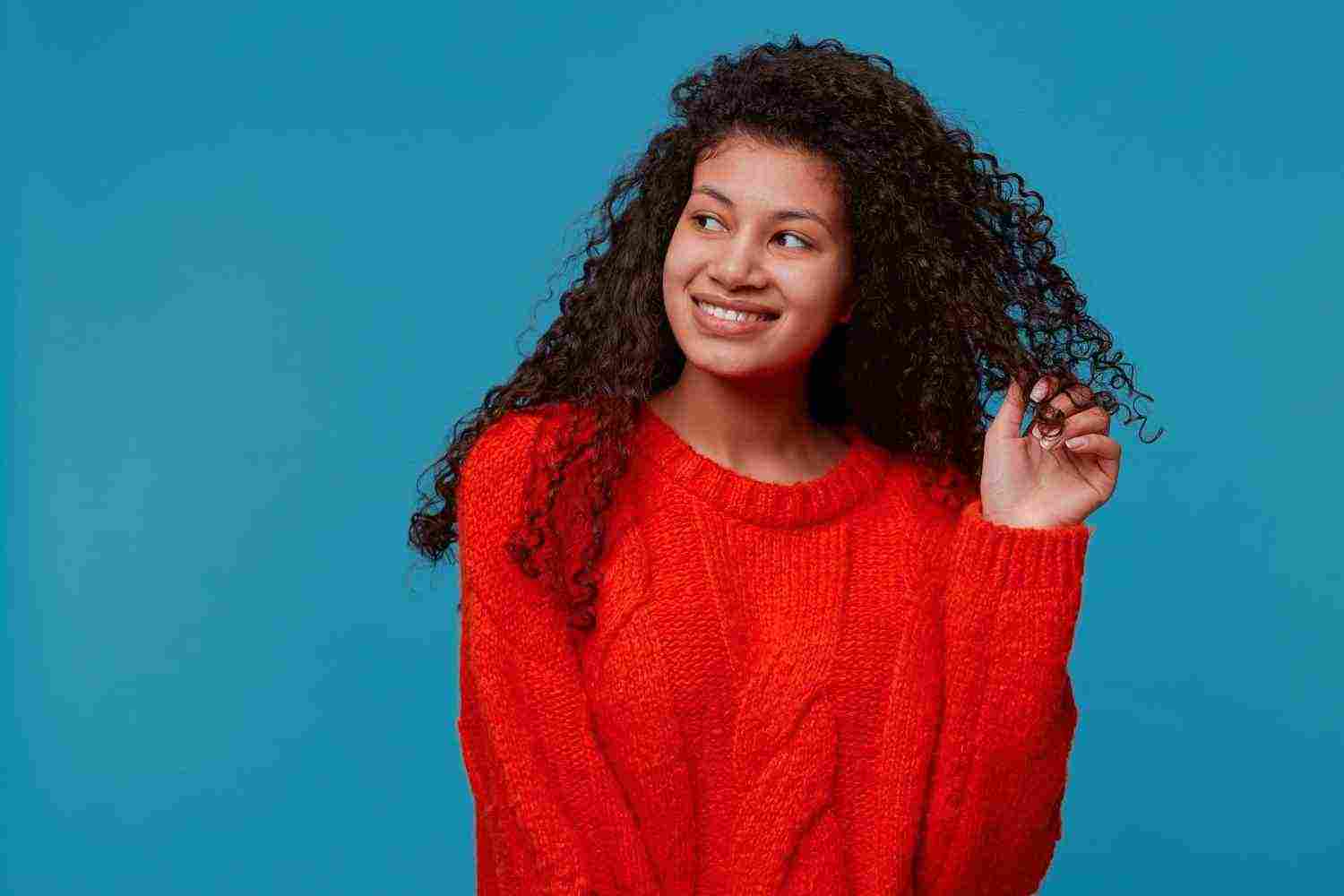 portrait beautiful lady with curly dark hair red knitted sweater holds strand hair her hand smiling