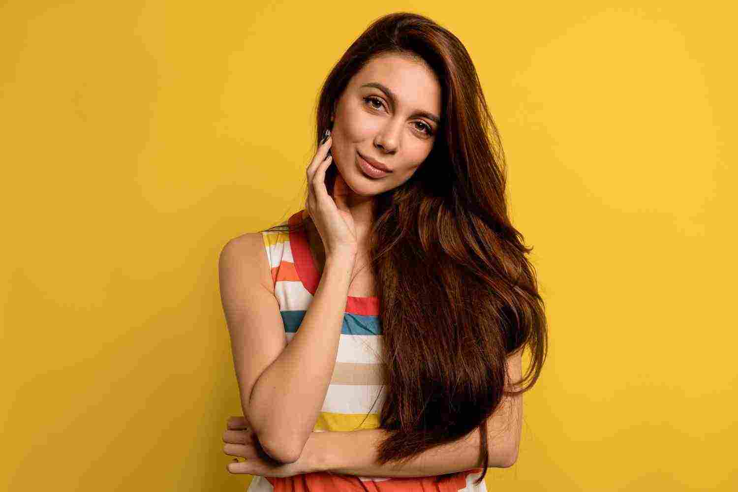 studio portrait pretty lady with long dark hair wearing bright summer dress posingwith happy emotions yellow wall