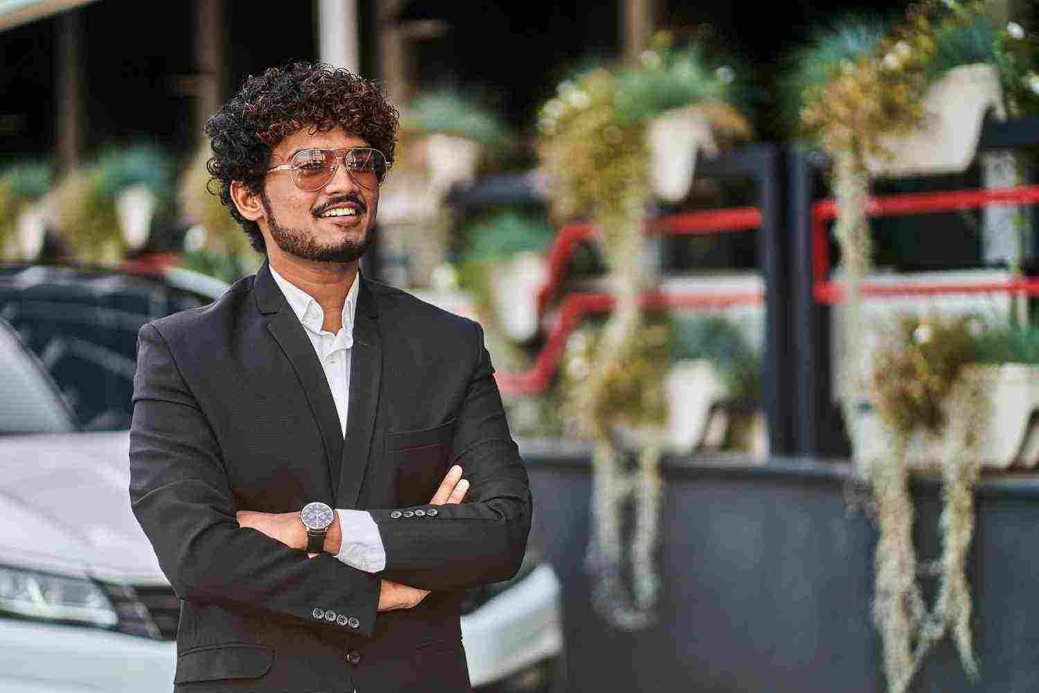 tall indian businessman with glasses near car black suit