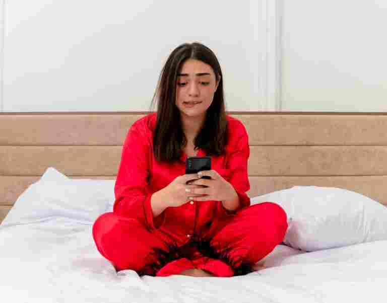 young beautiful woman red pajamas sitting bed using smartphone looking confused nervous bedroom interior light background