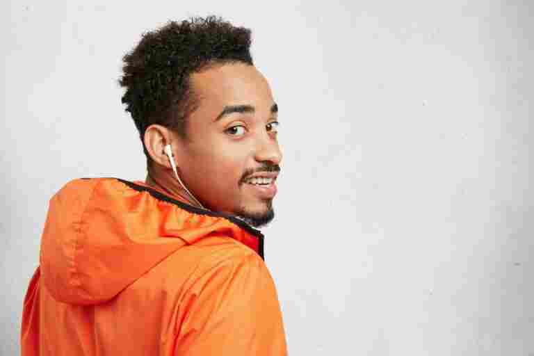 back view stylish afro american man wears orange anorak with hood walks alone enjoys pleasant melodies