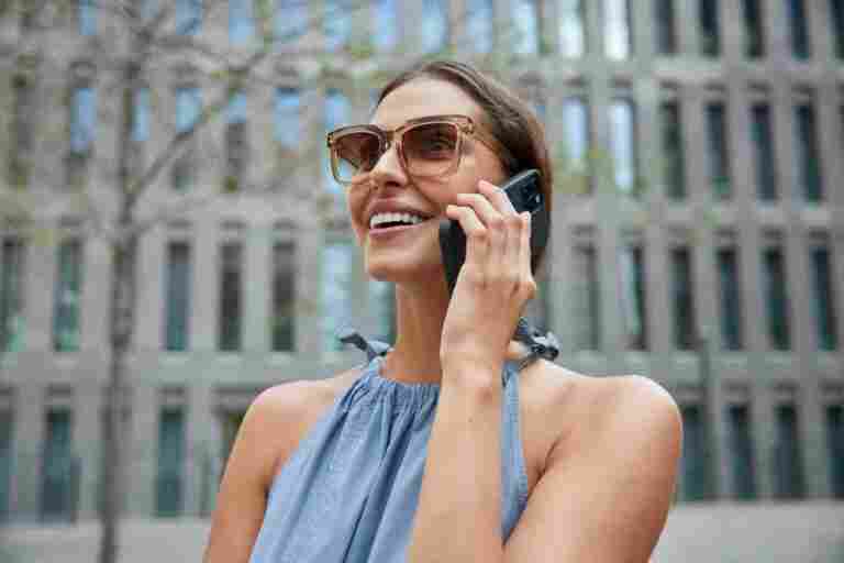 woman has telephone conversation roaming feels glad enjoys walks architectural city talks via phone wears sunglasses during sunny day poses outdoors