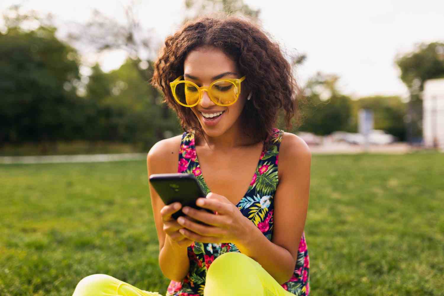 young stylish smiling woman using smartphone listening music wireless earphones having fun park