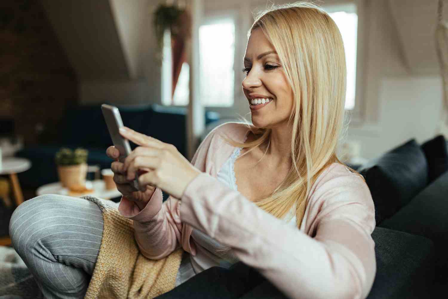 happy woman texting smart phone while relaxing living room