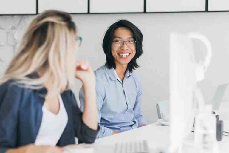 portrait long haired laughing asian man with blonde woman pleased chinese office worker blue shirt joking with female colleague workplace