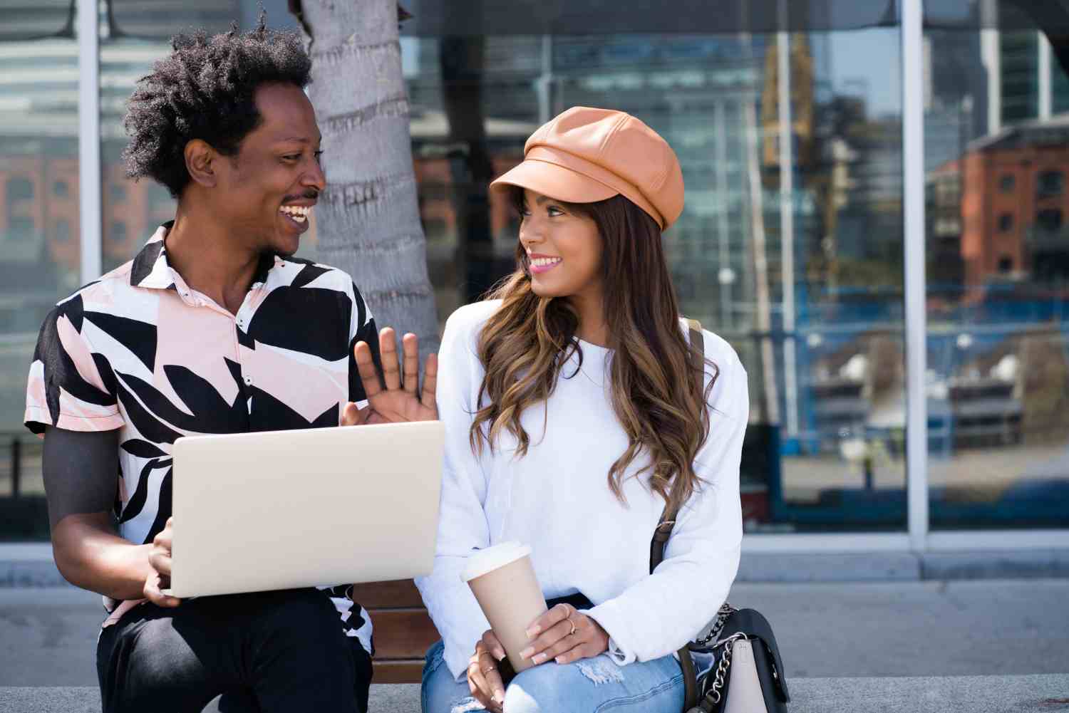 portrait young couple using laptop while sitting outdoors street