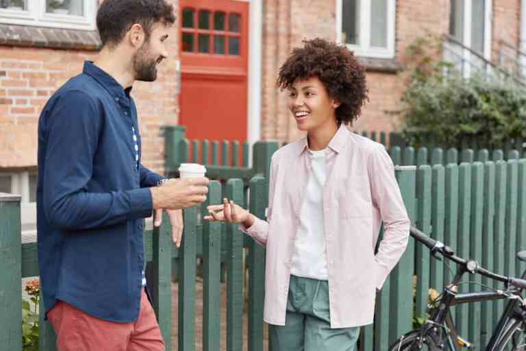 positive multiracial couple walk rural setting stroll during weekends drink takeaway coffee stand near fence have pleasant talk with each other