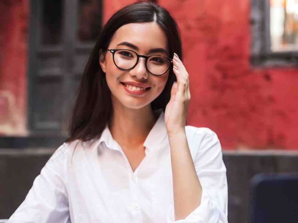 pretty smiling girl with dark hair white shirt eyeglasses happily looking camera with laptop notepad cozy courtyard cafe