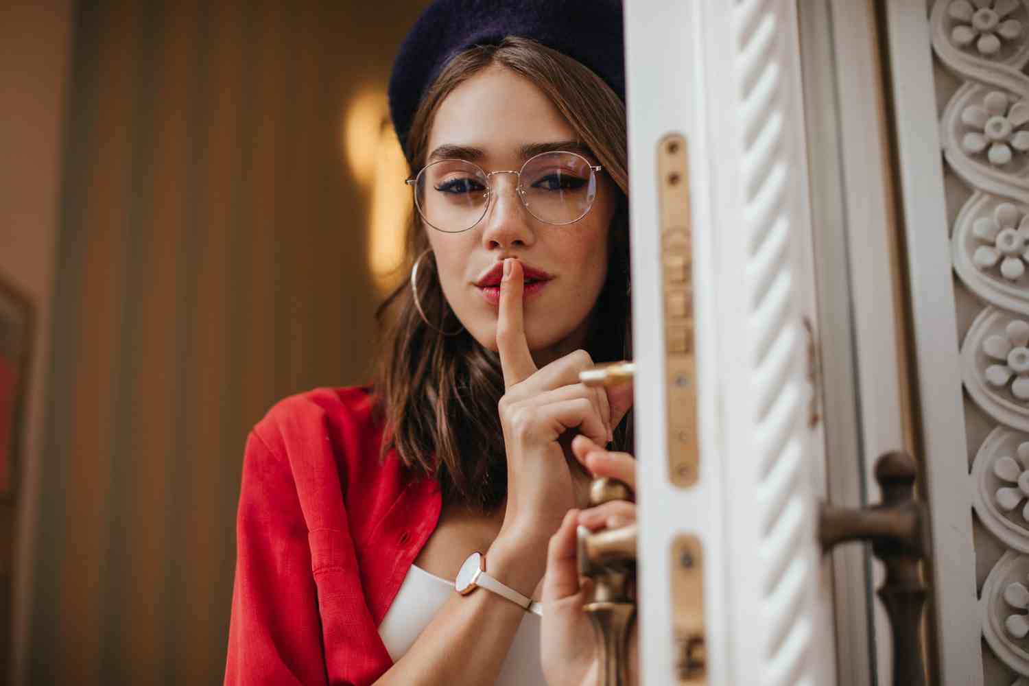 sexy lady with brunette hair red lipstick beret shirt stylish accessories posing holding index finger lips looking front opening white doors