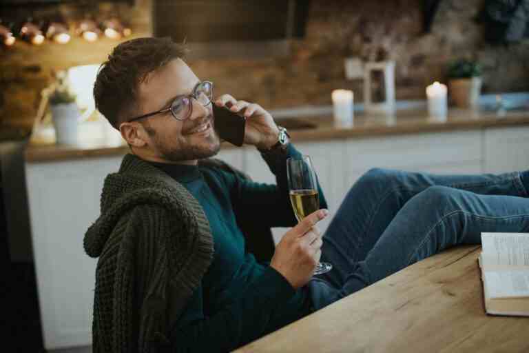 young happy man talking phone while drinking champagne home