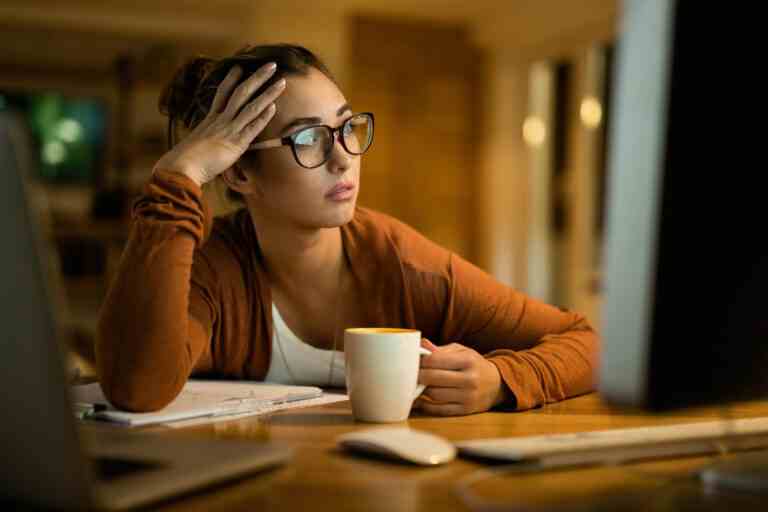 young pensive woman reading email desktop pc while working evening home 1