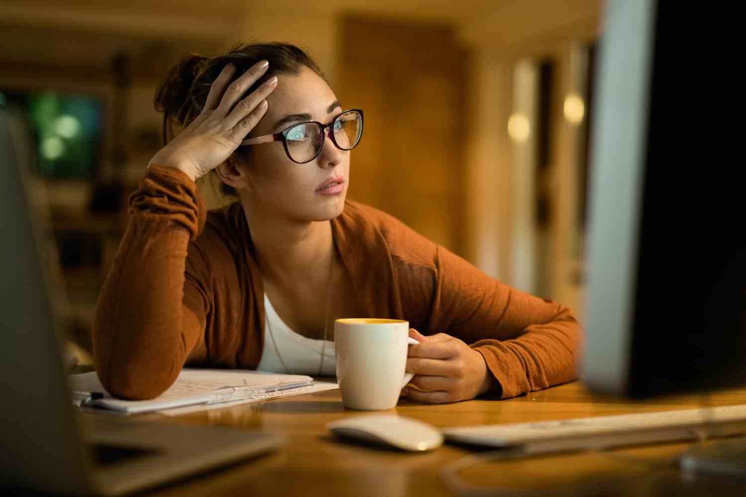 young pensive woman reading email desktop pc while working evening home