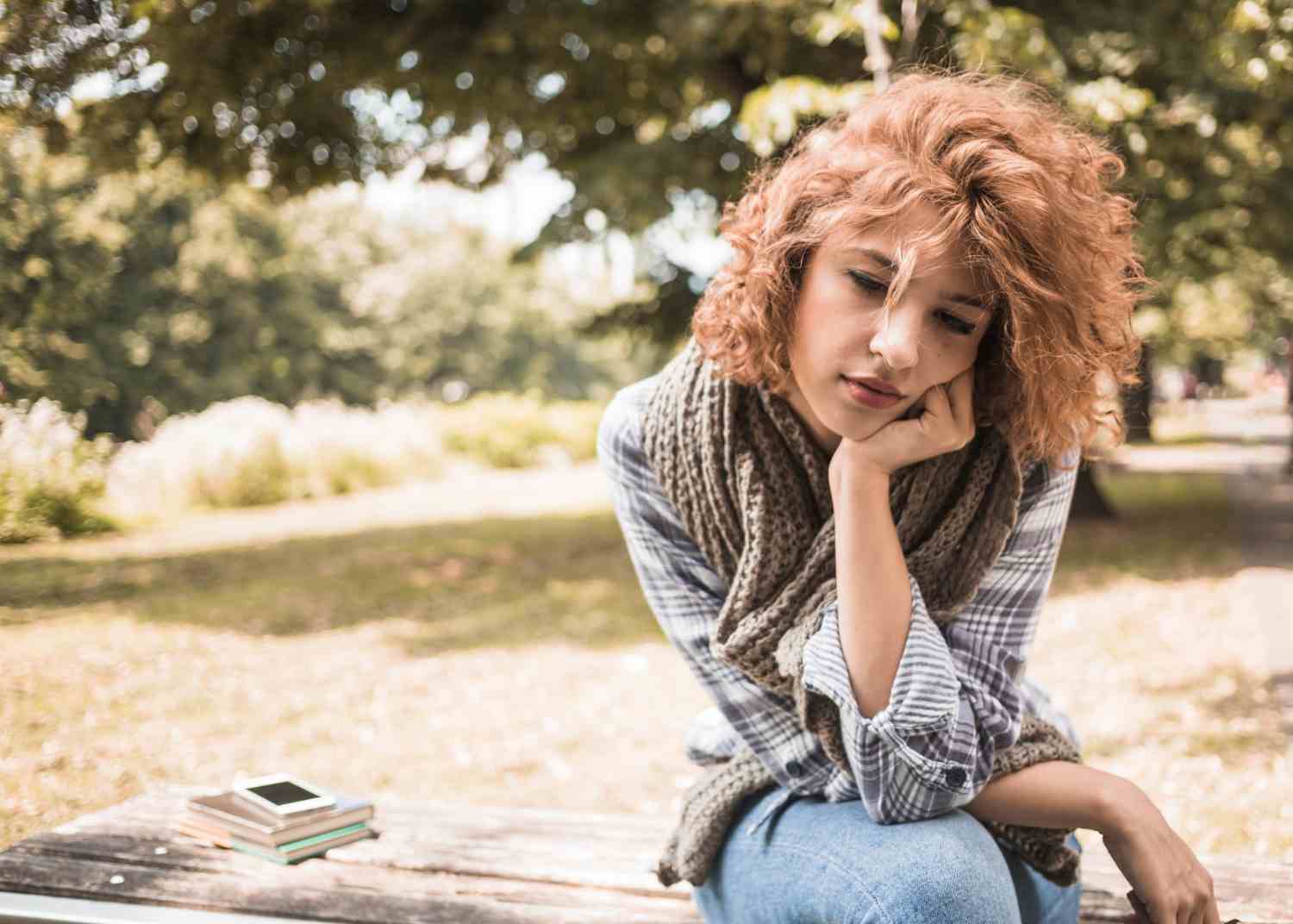 bored female sitting bench with books phone park