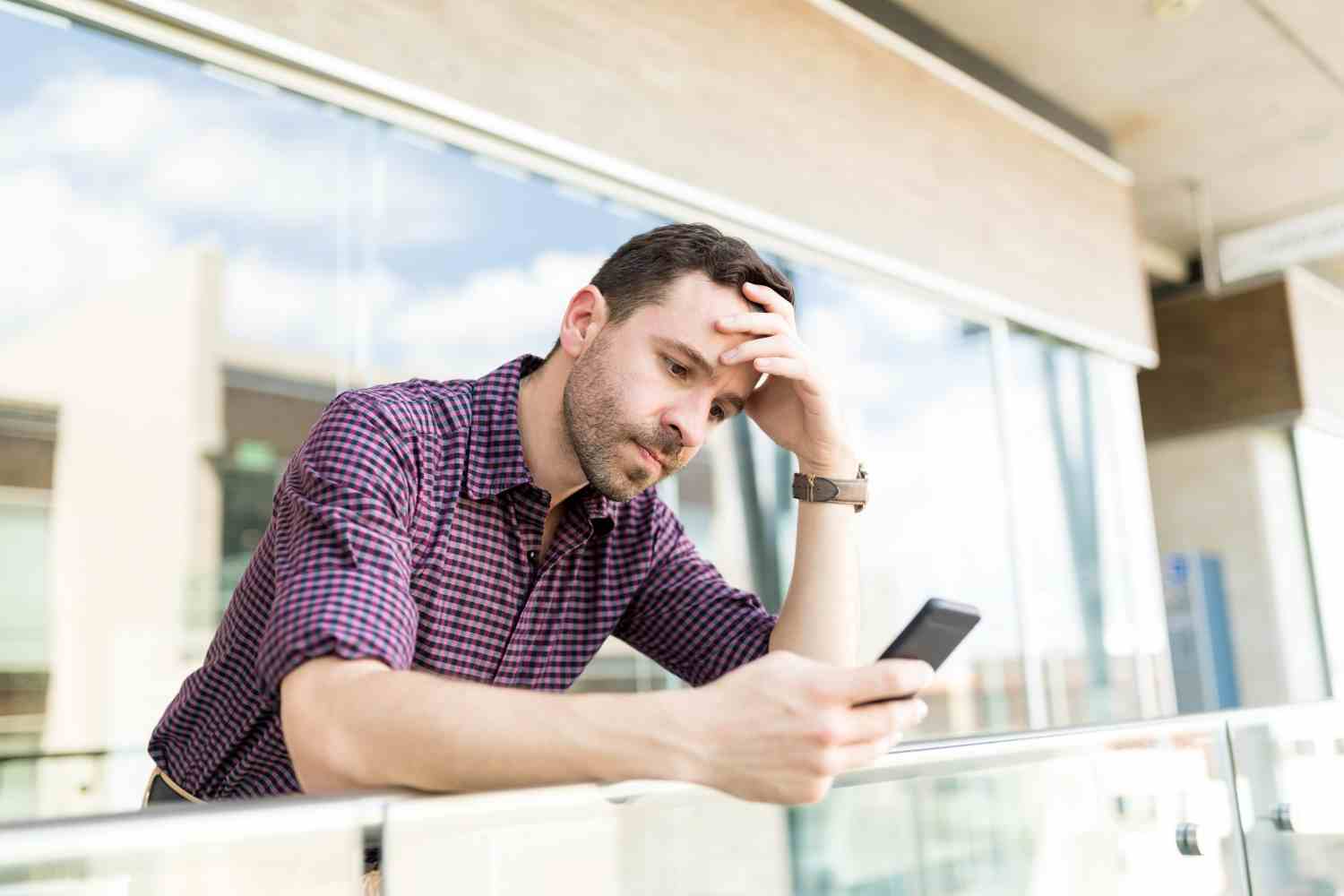 tensed man reading distressing news smartphone while leaning railing shopping mall
