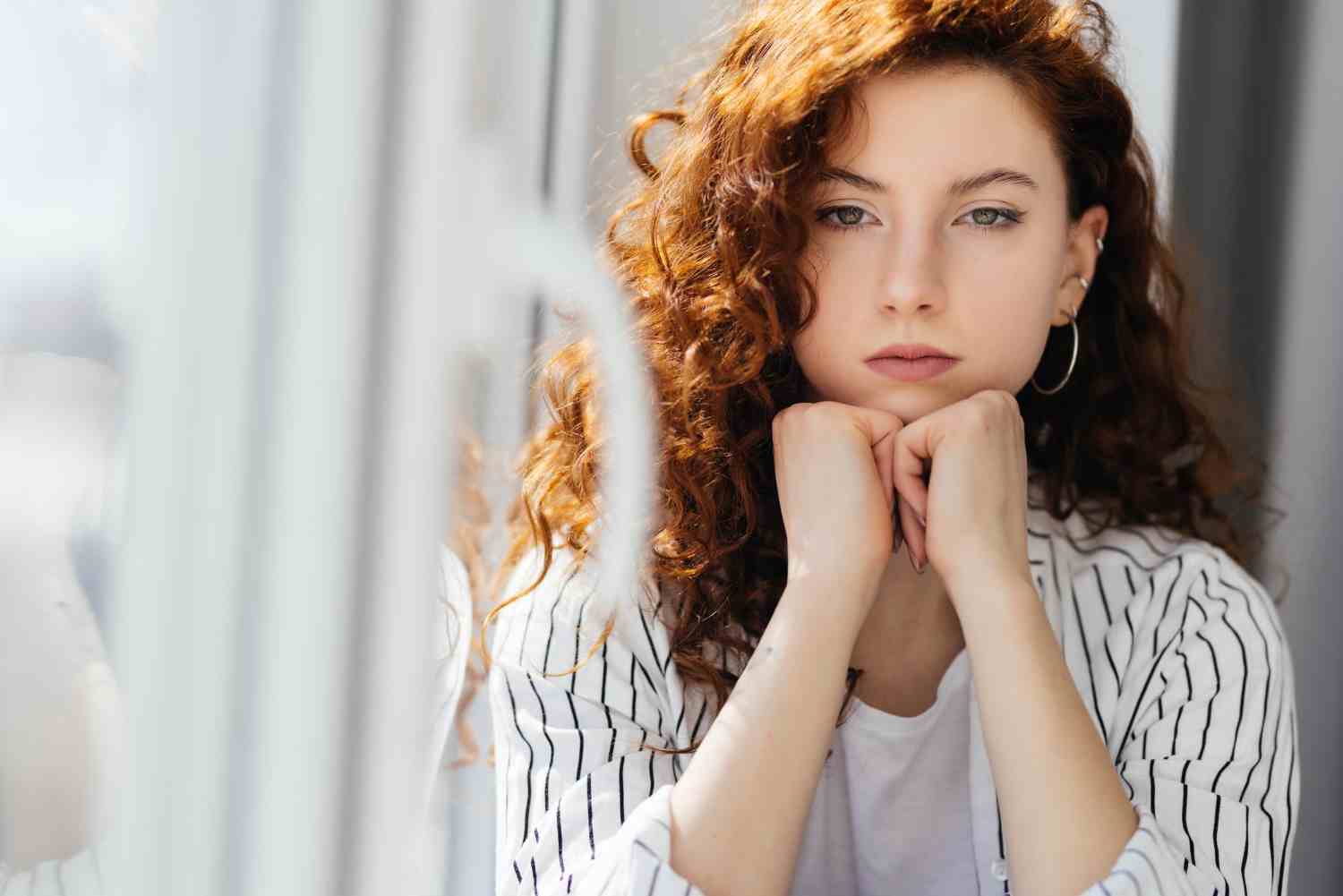 upset young woman shirt sitting windowsill home