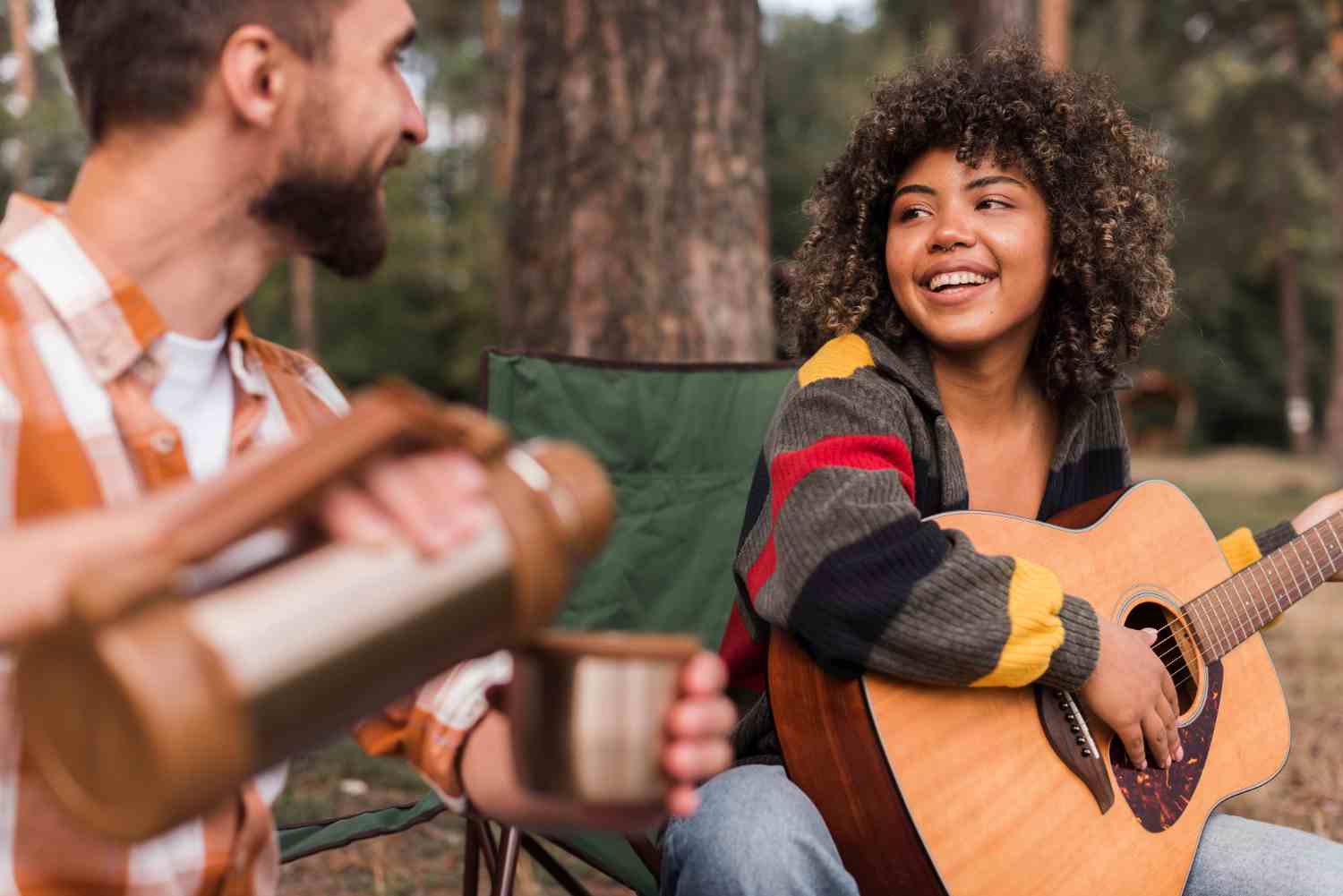 smiley couple enjoying camping outdoors with guitar hot drink